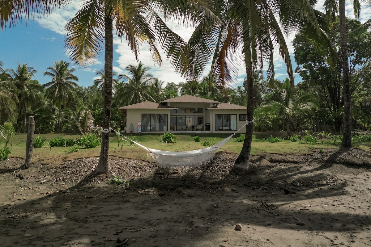 Casa Zola vista desde la playa, entre palmeras